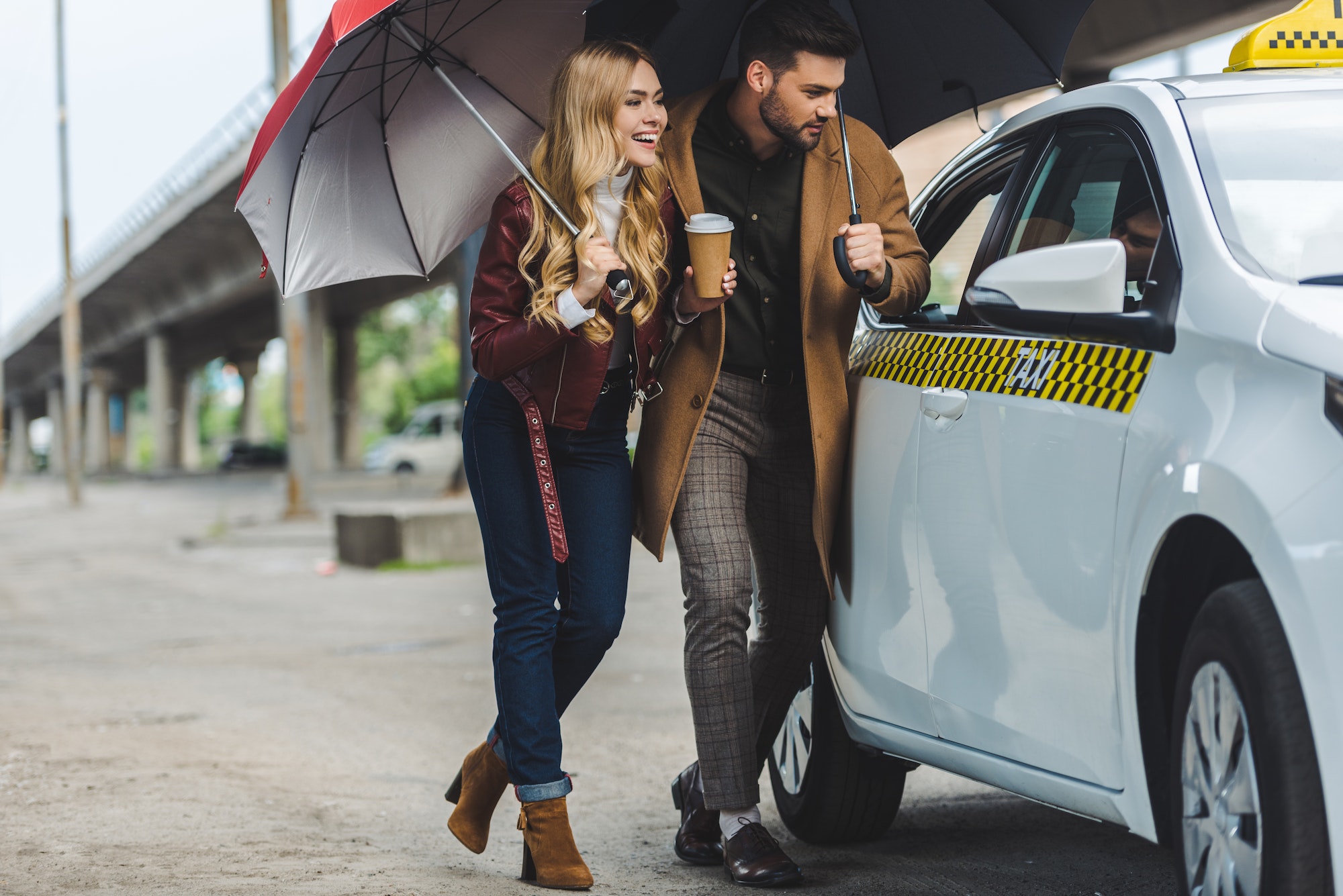 smiling young couple with umbrellas looking at taxi car